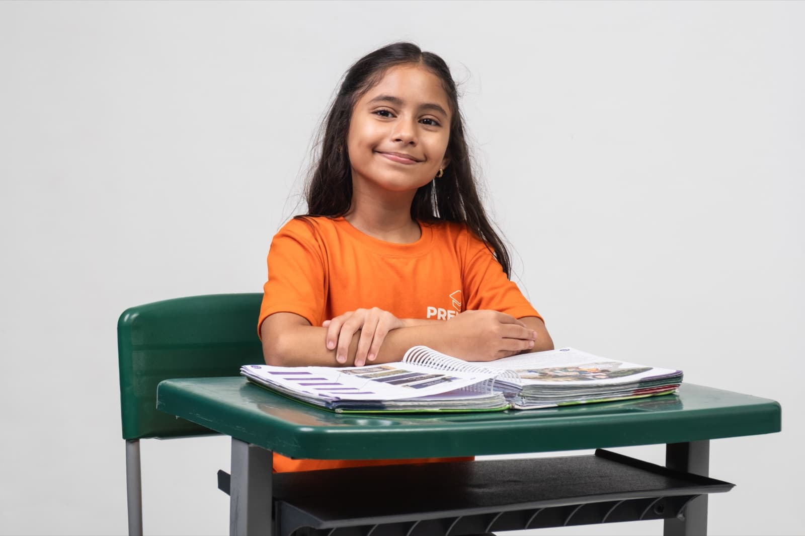 Aluna do Fundamental sorrindo na carteira, com o livro didático aberto