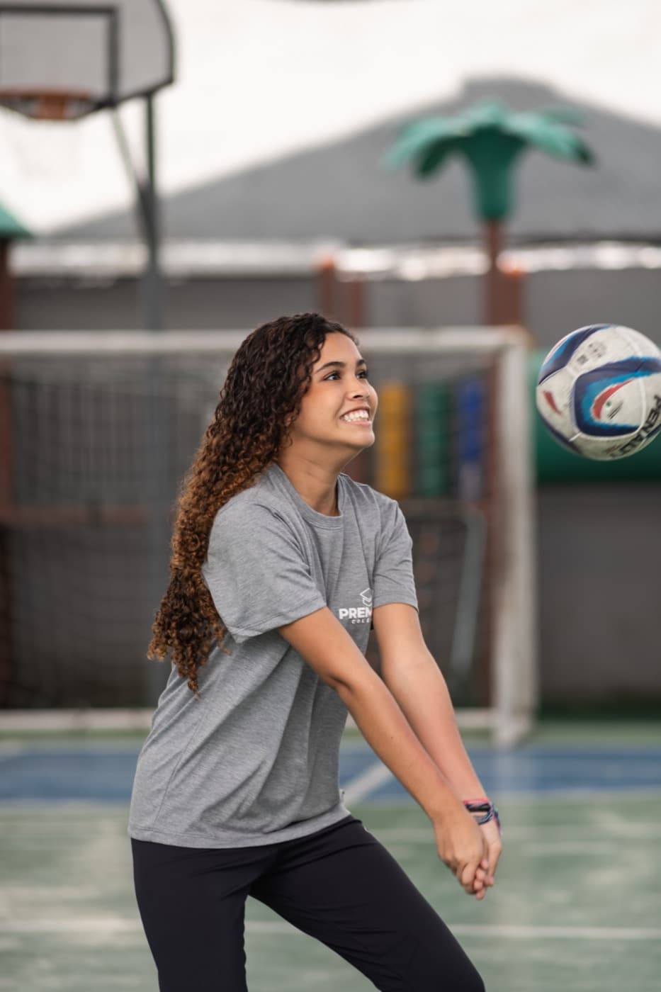 Aluna sorrindo ao receber a bola de vôlei na quadra do colégio